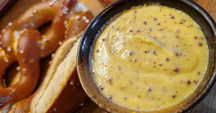 Close-up of creamy beer mustard sauce with visible mustard seeds in a rustic ceramic bowl, served alongside soft German pretzels.
