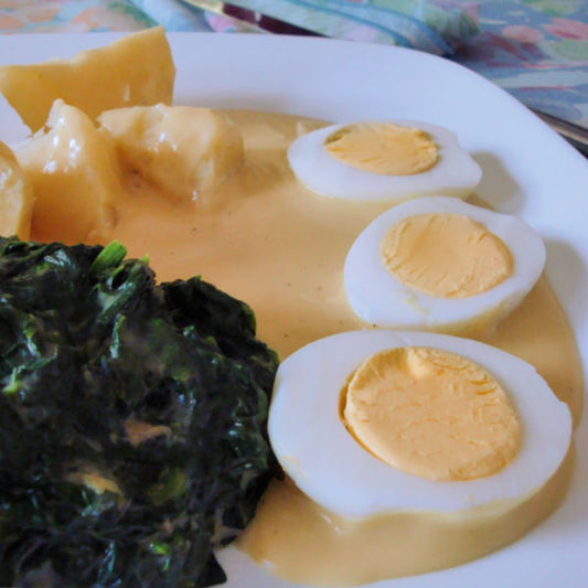 Plate of creamed spinach served with mashed potatoes and two fried eggs, showing the creamy texture and vibrant green color of the spinach.