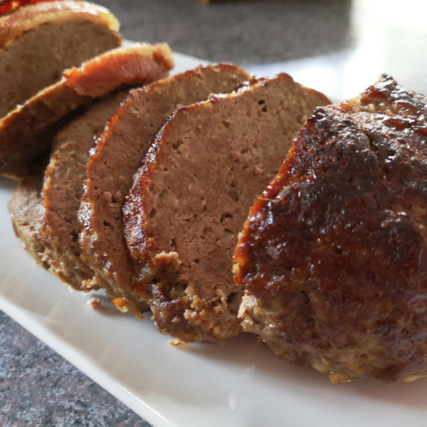 Close-up of juicy, sliced German meatloaf on a white serving plate.