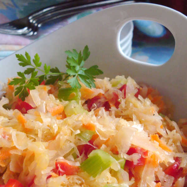Close-up of colorful sauerkraut salad with shredded carrots, red peppers, celery, and fresh parsley garnish in a white dish.