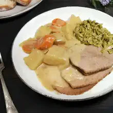 Plate of slow cooker beef pot roast with gravy, potatoes, carrots, and green beans.