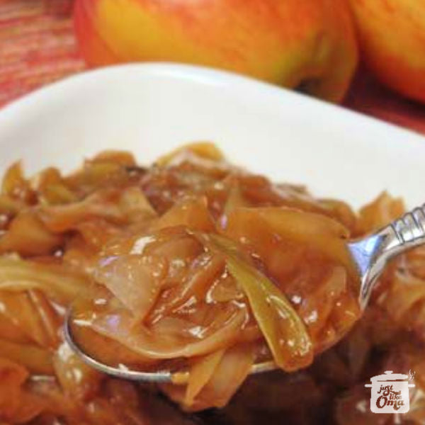 Close-up of a spoonful of caramelized braised cabbage served from a white bowl, with apples in the background.
